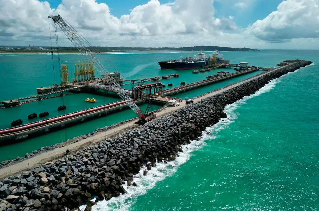 Aerial view of a port breakwater and tanker berths, with a crawler crane at work
