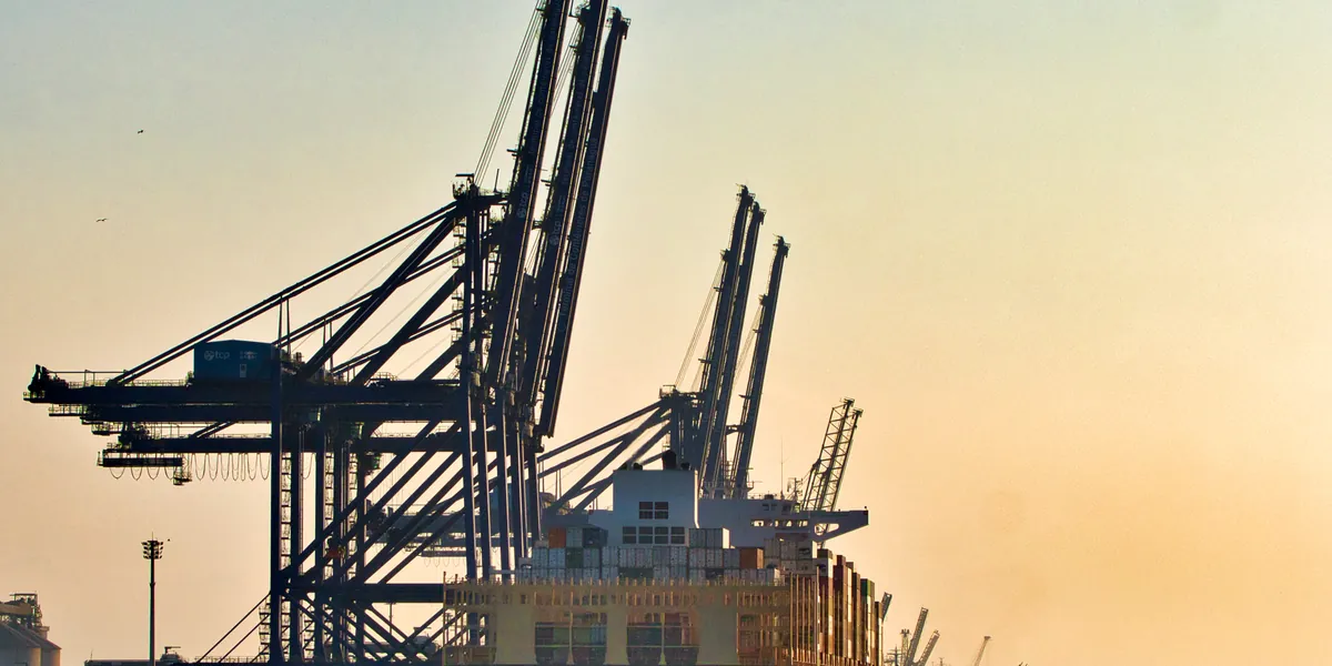 Container cranes at the Paranaguá container terminal at sunset, with a container ship alongside.